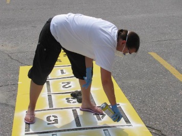 Woman painting playground stencils on pavement
