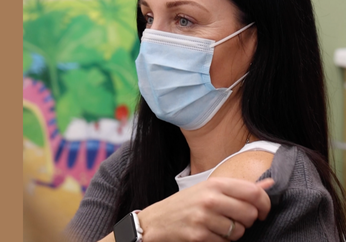 Image of someone rolling down cardigan sleeve, preparing to receive vaccine