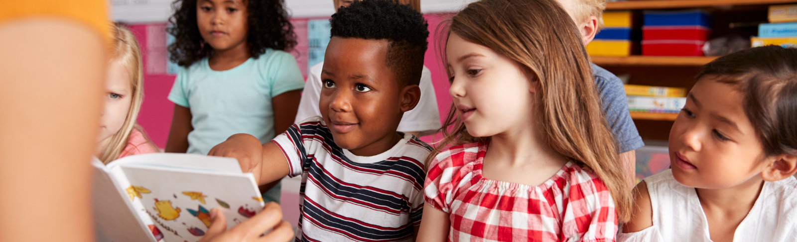 Image of young children sitting on classroom floor, learning with teacher and book