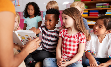 Young children sitting on classroom floor, learning with teacher and book