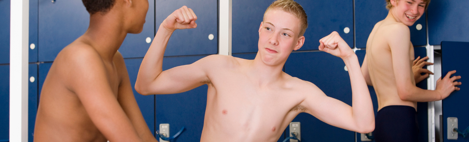 Image of teens in a locker room, one flexing muscles while making eye contact with other teen