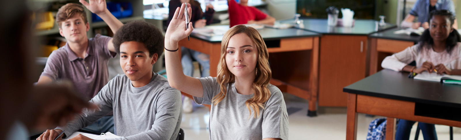 Teens sitting in a classroom, some raising their hands