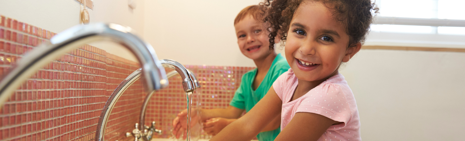 Two children smiling by sinks in a washroom