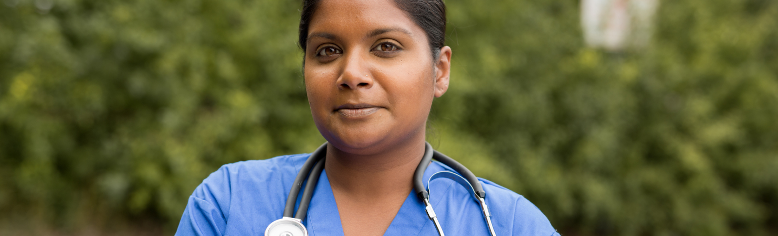 Image of a person standing outside, wearing scrubs, a stethoscope around their neck