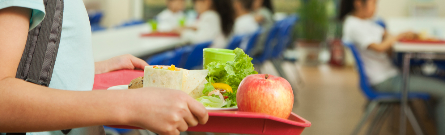 Image of a tray of healthy foods being carried through a cafeteria setting