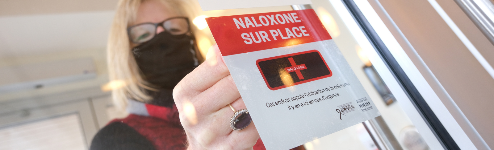Image of a professional displaying a sign on window to indicate presence of naloxone