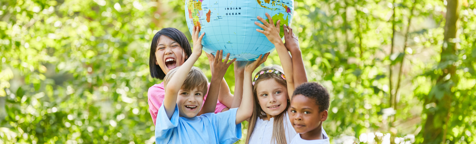 Four children surrounded by leafy trees, holding up a globe