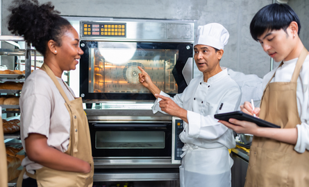 A chef giving a lesson to two others by professional kitchen oven