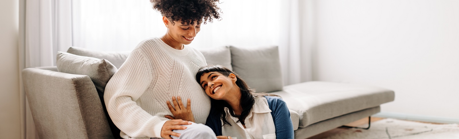 Pregnant woman sitting with another woman touching her belly