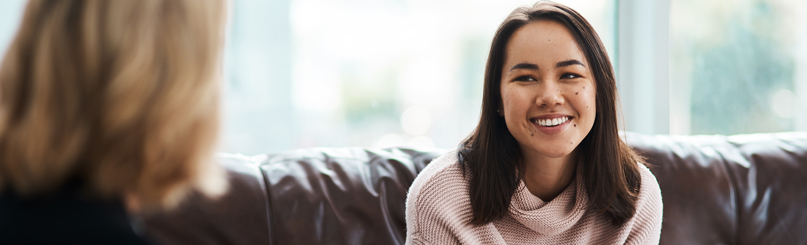 Lady sitting on a couch speaking to another lady.
