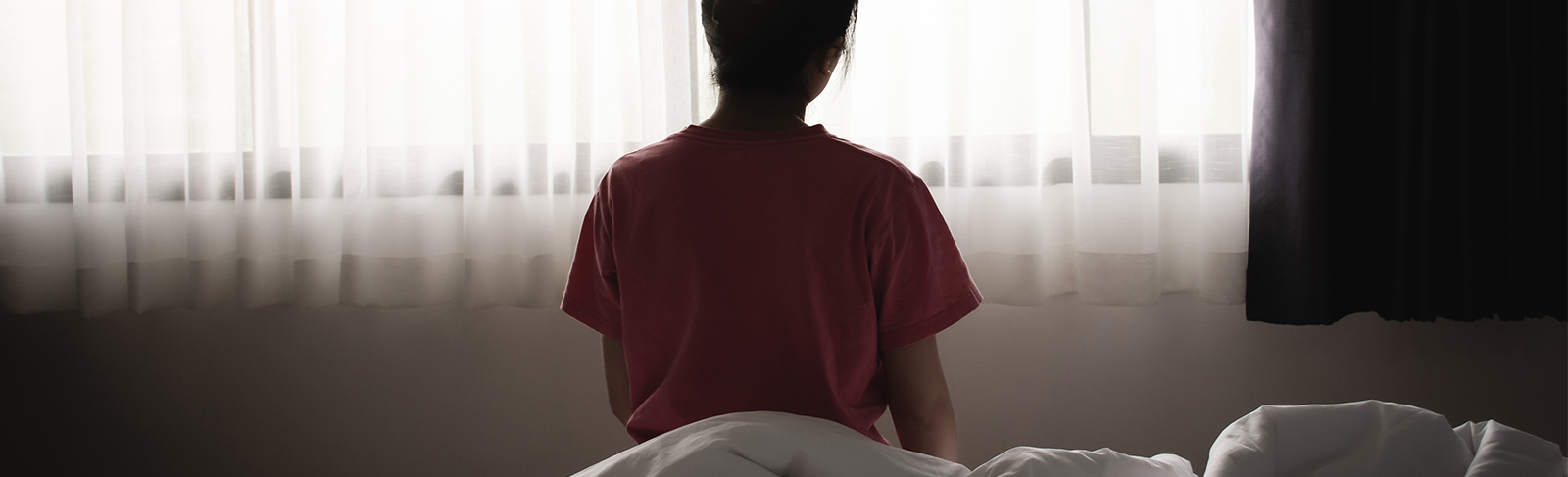 Women sitting facing a window, we can only see her back.