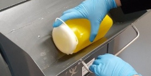 Image of gloved hands submitting a biohazard container into a sharps disposal bin
