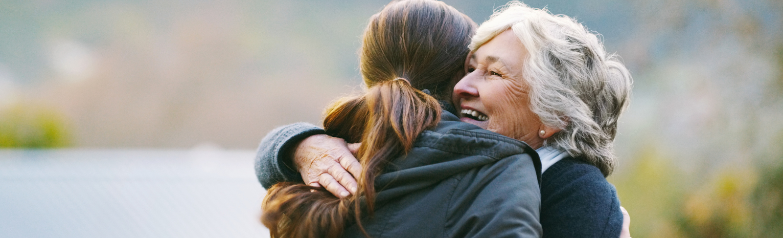 Image of an older person being hugged by a younger person in an outdoor setting