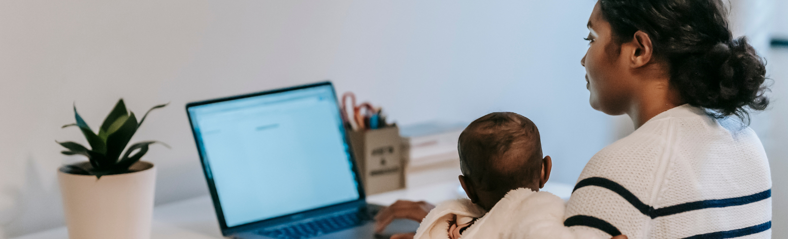 Image of a mother and baby sitting at home desk, looking at open laptop