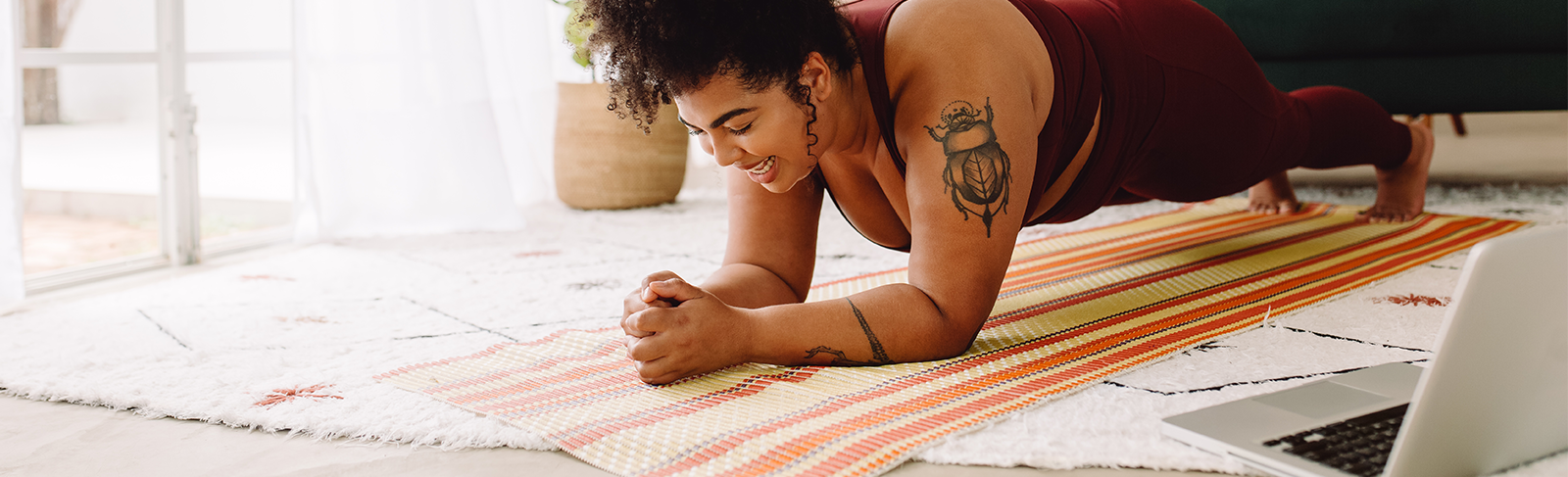 Lady in maroon doing an online workout in a plant position