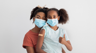 Image d'un parent et d'un enfant portant des protections faciales. Un bandage est posé sur le bras supérieur de l'enfant.
