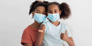 Image of a parent and child wearing face coverings. A bandage is on the child's upper arm.