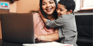 Image of a mother using laptop and smiling while receiving a hug from child