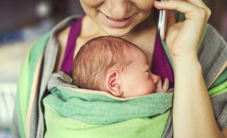 Person holding phone to ear with baby on chest