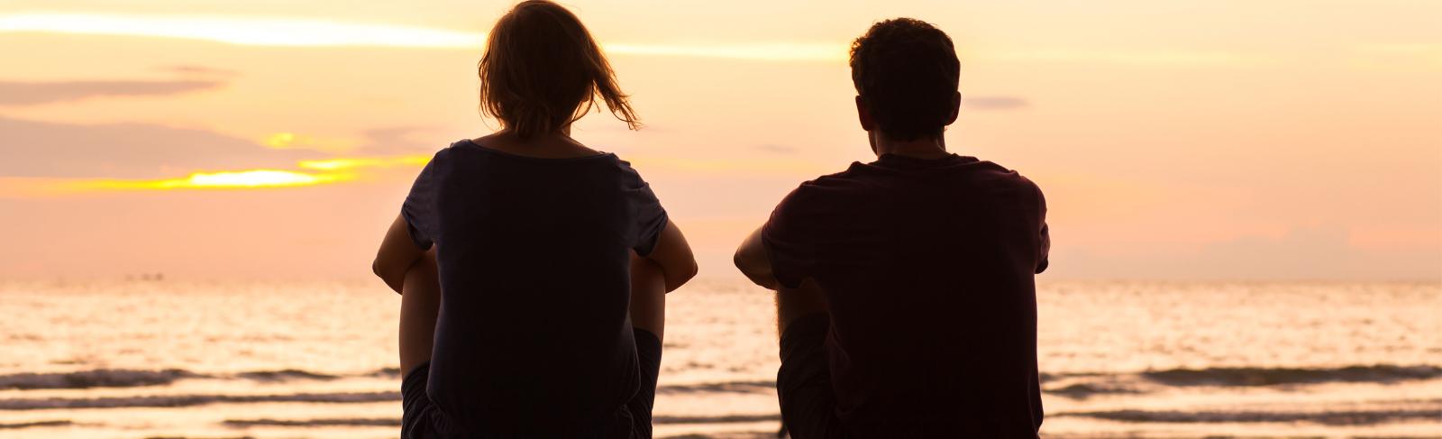 Silhouettes of two people sitting side-by-side on beach