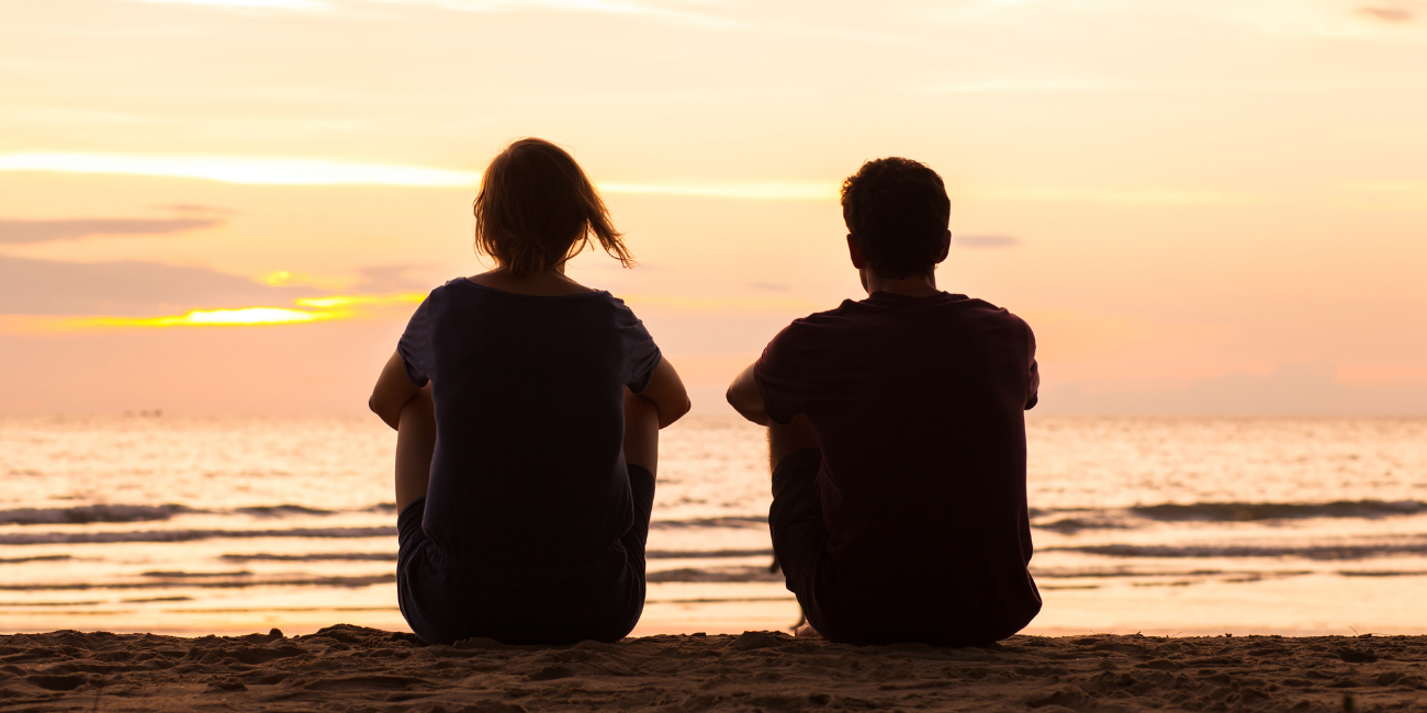 Two human silhouettes sitting and watching sunset on beach