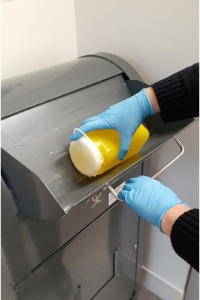 Image of a biohazard container being dropped into a community sharps bin by someone wearing gloves.