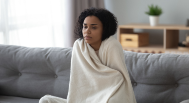 Unwell person wrapped in blanket, sitting on couch