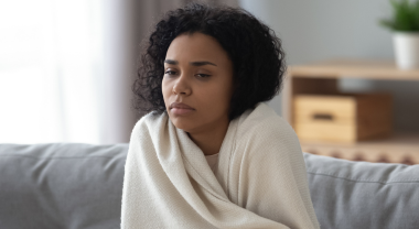 Unwell person wrapped in blanket, sitting on couch