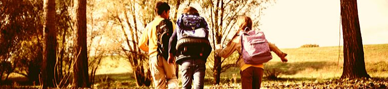 three children wearing back packs walking to school in a wooded area