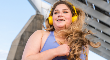 Happy woman running outdoors on sunny day, wearing headphones