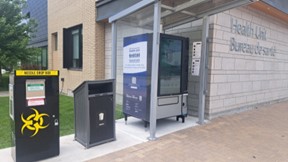 Digital vending machine next to a waste bin and community sharps bin, outside a building labelled 'Health Unit'