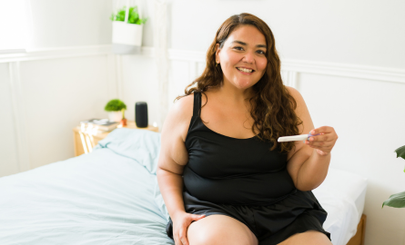 Female-presenting individual smiling and holding pregnancy test