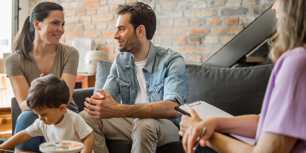 Young couple with active toddler having conversation in home setting with older aduly