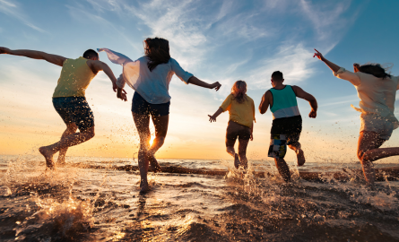 Image of young people running through shallow lake water toward sunset