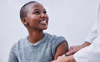 Image of a person smiling and looking upward toward doctor as they place band-aid on the person's upper arm