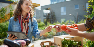 Female-presenting individual making a transaction with customer at a farmer's market stand