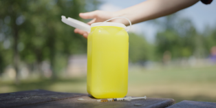 Image of a biohazard container outside, with hand positioned to close open lid.