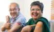 Two adults smiling and pointing to bandage on upper arms