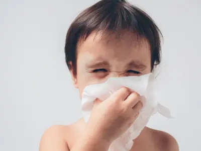 Young child sneezing into a tissue