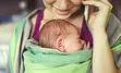 Person holding phone to ear while carrying baby in carrier