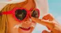 Little girl wearing hat and sunglasses; adult hand applying sunscreen to her nose